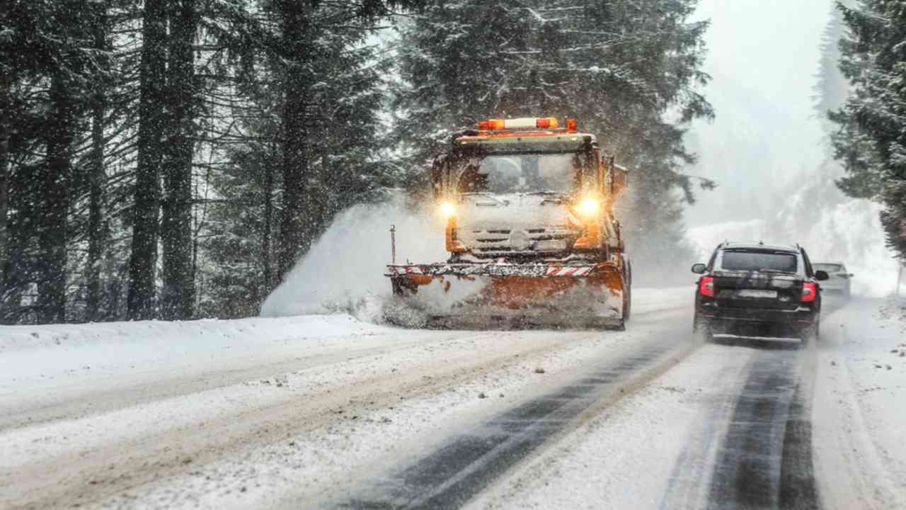 Snežný pluh odhŕňa čerstvý sneh na zasneženej ceste počas zhoršeného zimného počasia.