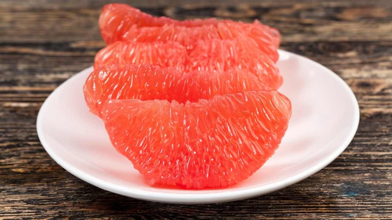 Rozpolený ružový grapefruit položený na kuchynskej doske.