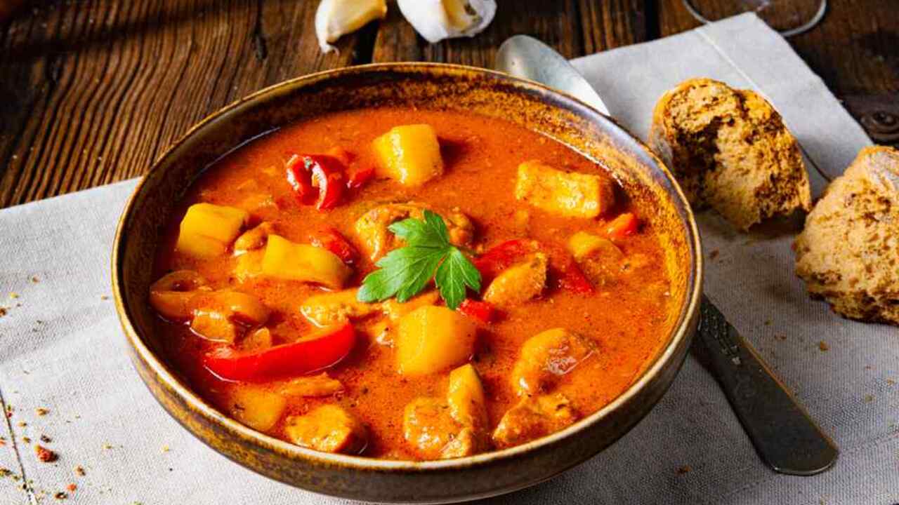 Maďarský guláš v miske so zemiakmi, paprikou a kúskami mäsa, podávaný s čerstvým chlebom.