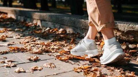 Osoba kráča po chodníku pokrytom jesenným lístím počas prechádzky