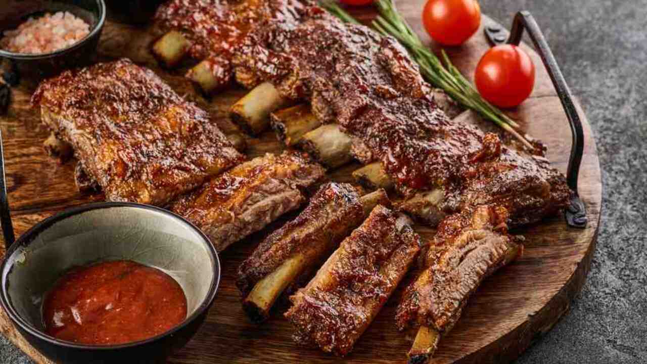 Pečené bravčové rebrá s omáčkou a cherry paradajkami servírované na drevenej doske.