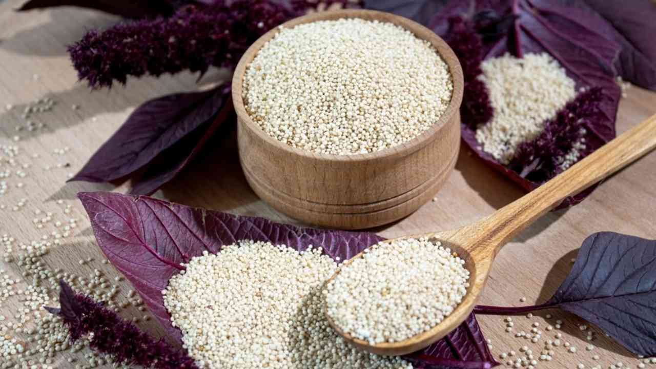 Drevená miska s amarantom a fialovými listami rastliny amarant, položená na svetlom drevenom stole.