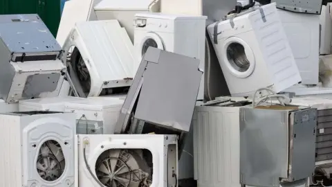 Hromada vyradených práčok a domácich spotrebičov pripravených na spracovanie elektroodpadu.