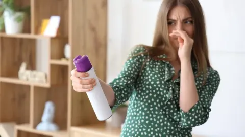 Žena si zapcháva nos a používa sprejový osviežovač vzduchu, ktorý jej zjavne prekáža svojou vôňou