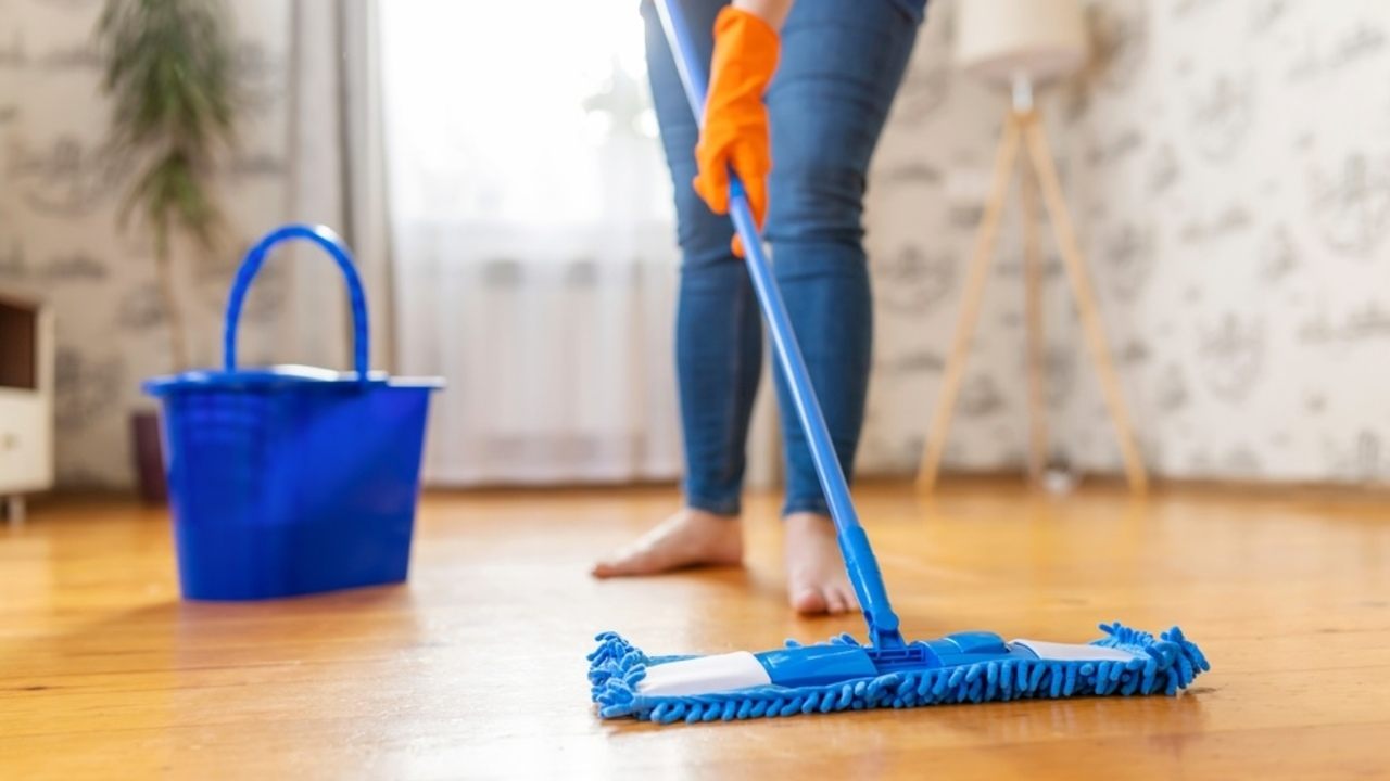 Osoba umývajúca podlahu modrým mopom v domácnosti, ilustrujúca správnu techniku čistenia podlahy.