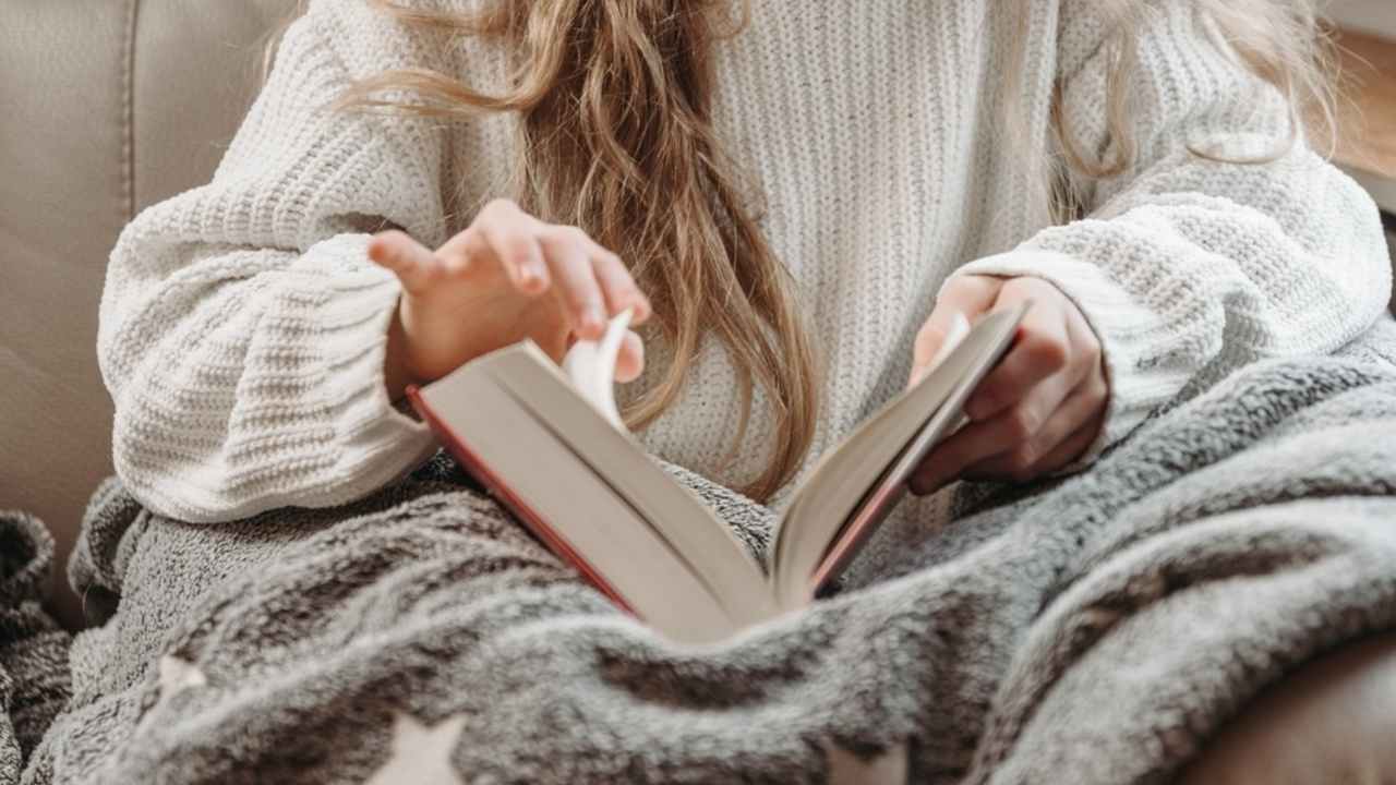 Žena číta papierovú knihu v pohodlnom prostredí pri dennom svetle.