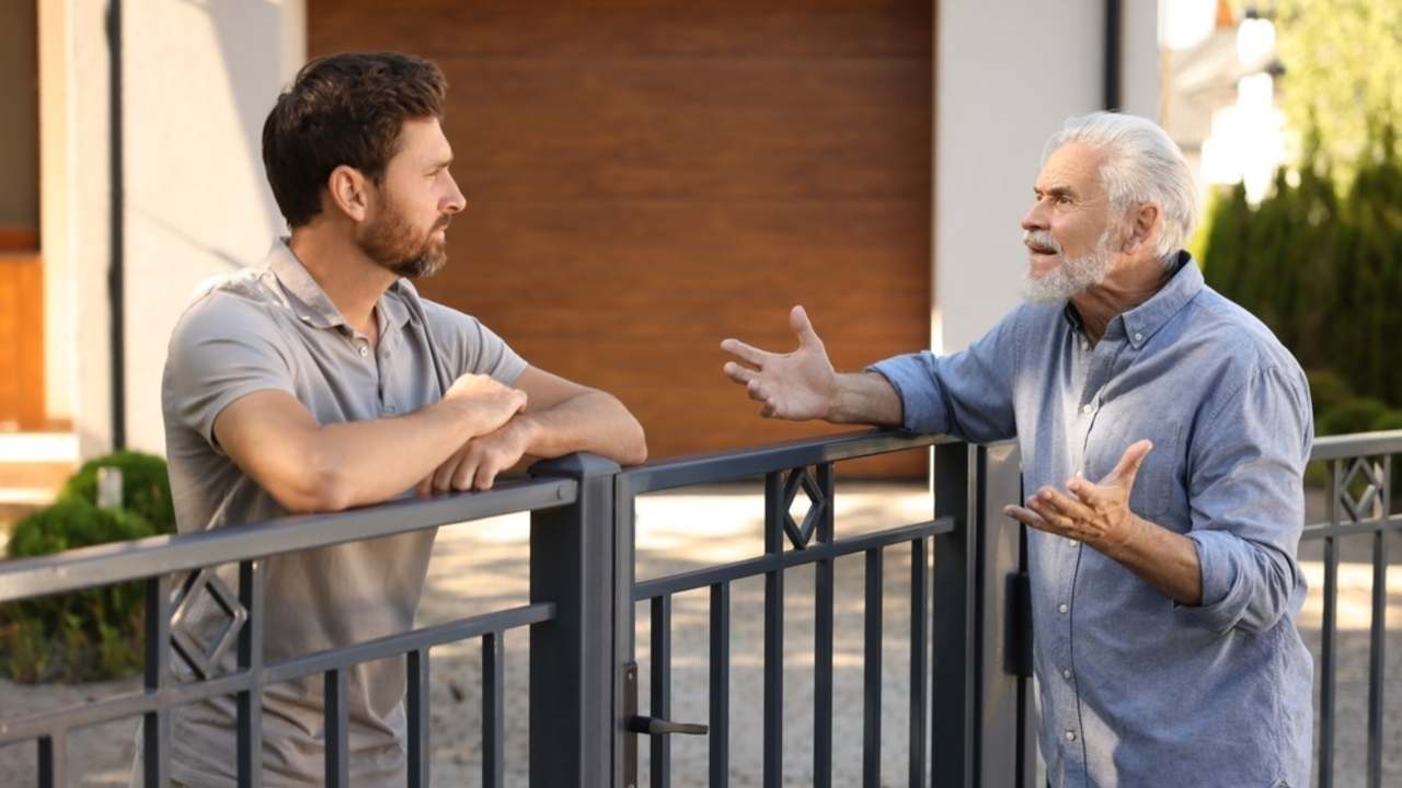 Susedia diskutujú pri plote o plánovanej stavbe.