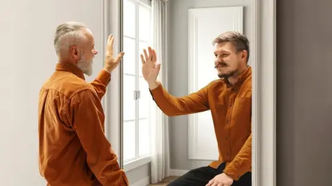 Starší a mladší muž si navzájom kývajú v zrkadle, symbol rýchleho plynutia času a vnímania veku