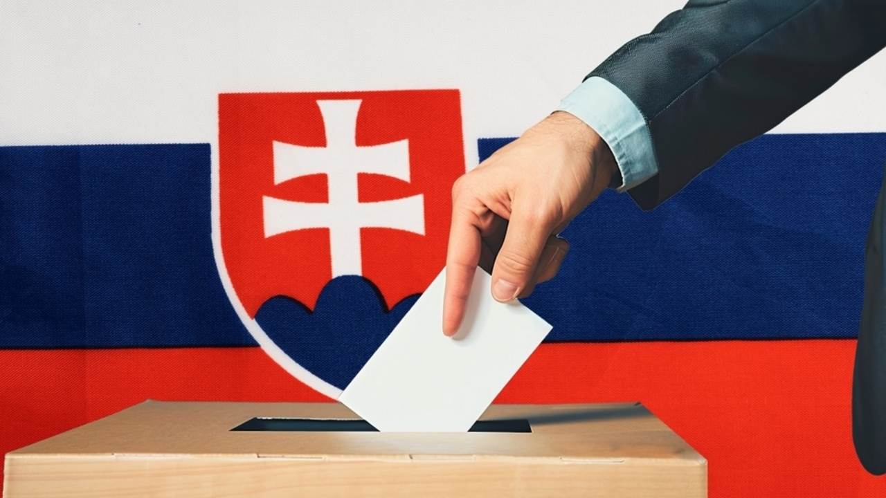 Ruka drž&iacute; volebn&yacute; l&iacute;stok vo volebnej urne na pozad&iacute; slovenskej vlajky. Ľudia vhadzuj&uacute; volebn&eacute; l&iacute;stky do volebnej urny na pozad&iacute; slovenskej vlajky. Voľby na Slovensku.