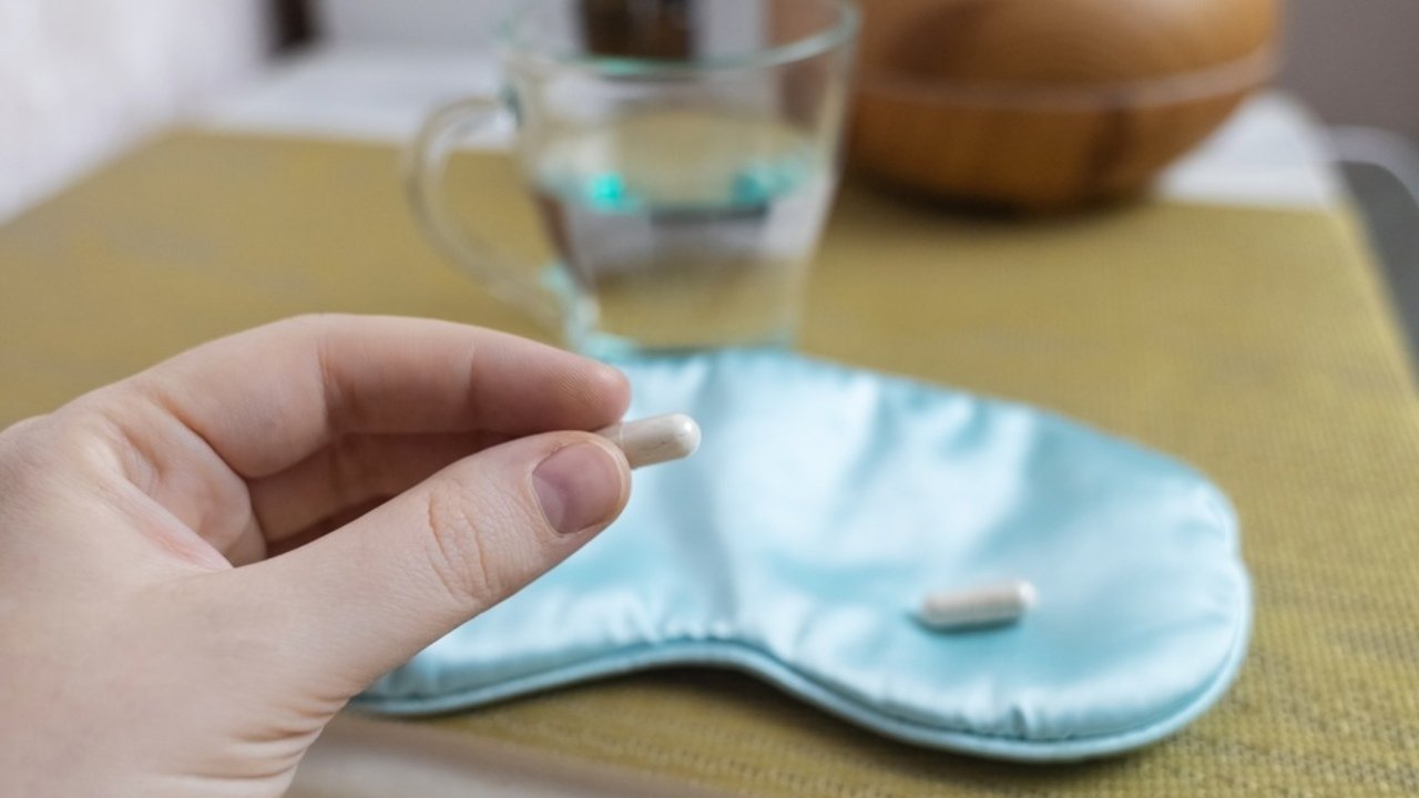 Tablety melatonínu položené na nočnom stolíku vedľa postele.