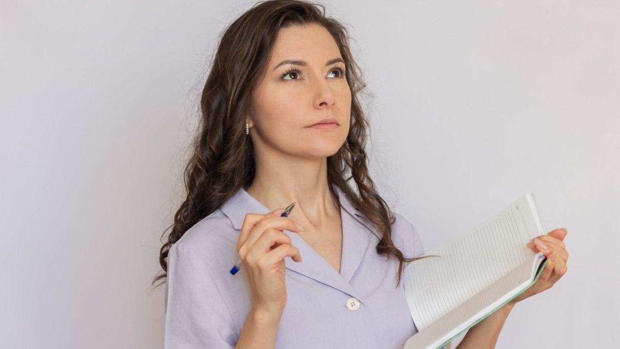 Premýšľajúca žena s poznámkovým blokom a perom, pôsobiaca pokojne a sústredene – symbol organizovanosti a plánovania.