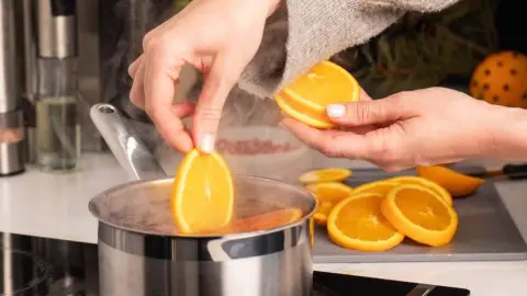 Plátky pomaranča vkladané do vriacej vody v hrnci, priprava domáceho voňavého osviežovača.