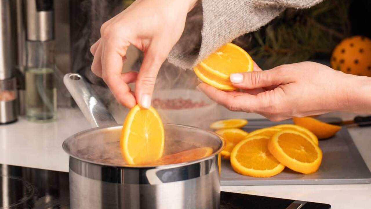 Plátky pomaranča vkladané do vriacej vody v hrnci, priprava domáceho voňavého osviežovača.