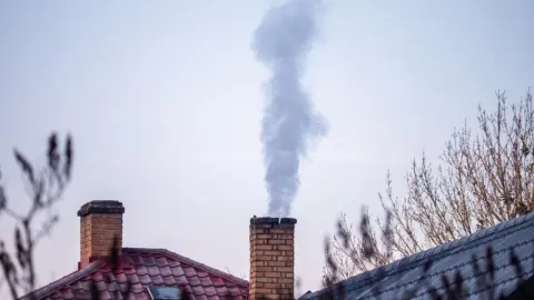 Dym stúpajúci z komína rodinného domu na pozadí jasného zimného neba.