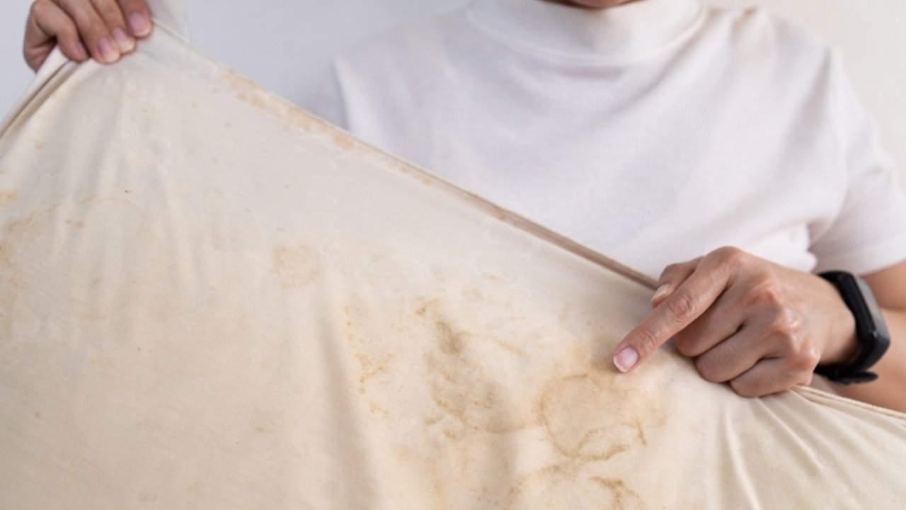 Žena drží vankúš so silnými žltými škvrnami a ukazuje na ne prstom