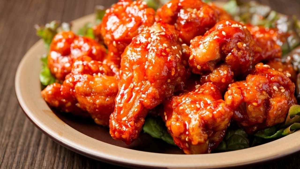 Kórejské vyprážané kuracie kúsky obalené v lesklej pikantno-sladkej glazúre na tanieri.
