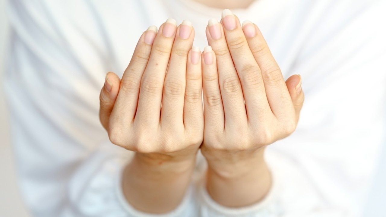 Detail ženských rúk s prirodzene upravenými nechtami na stole v dennom svetle.