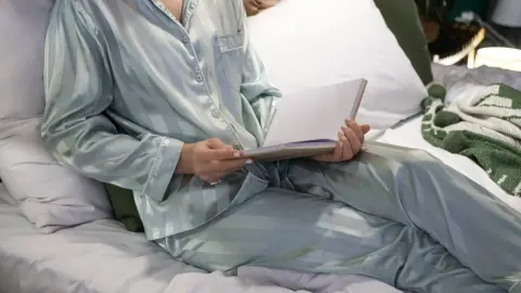 Žena číta knihu v posteli počas večerného rituálu.