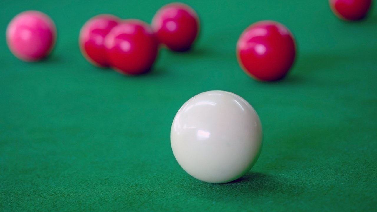 Snookerové gule na zelenom stole, biela guľa v popredí a červené gule v pozadí.
