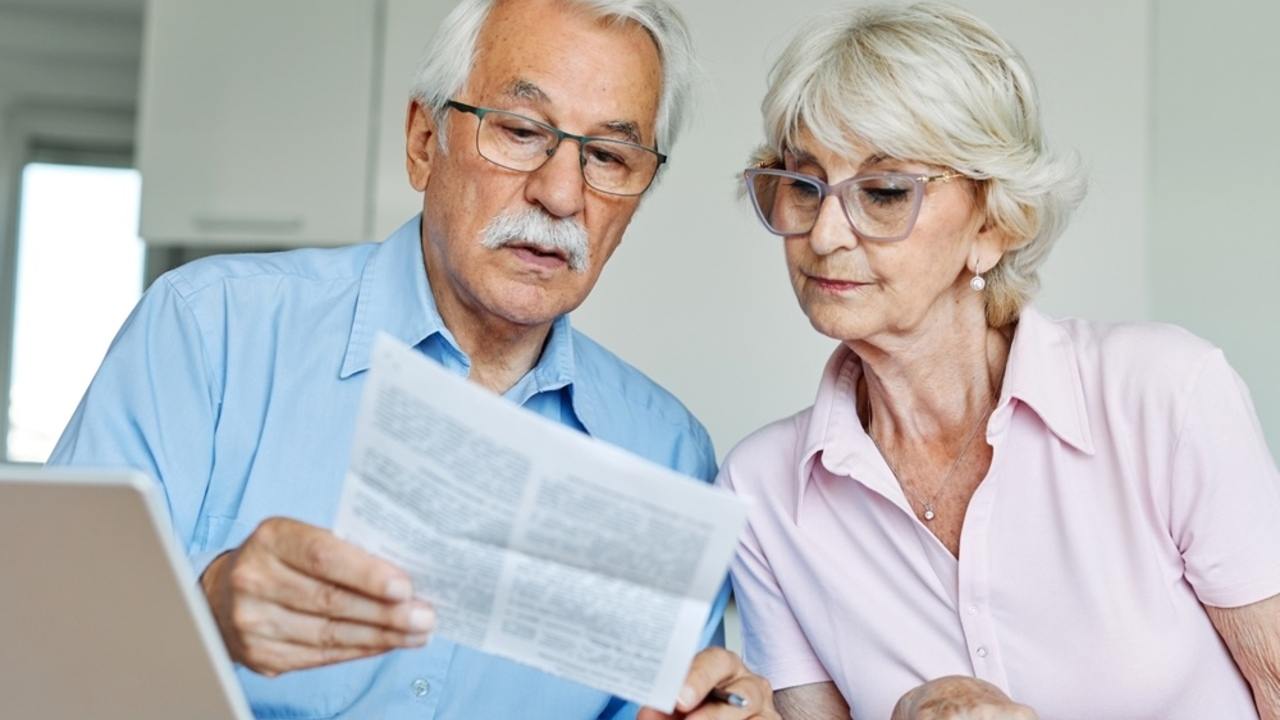 Starší manželský pár prezerá dokumenty o dôchodku doma pri stole.