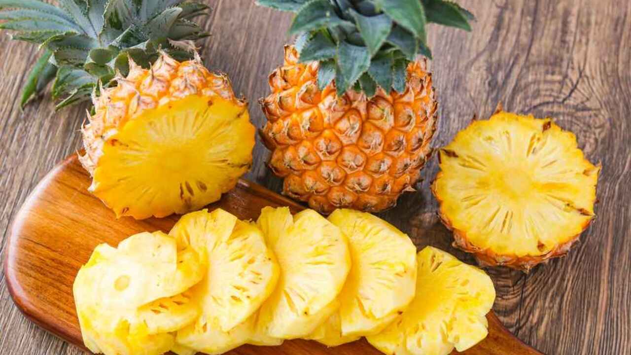 Nakrájaný čerstvý ananás na doske, celý ananás a plátky tropického ovocia