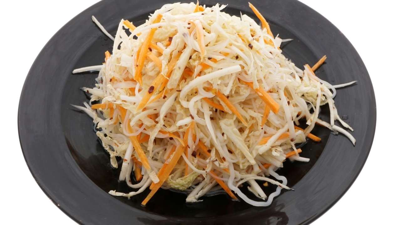 Čínsky šalát z kapusty a mrkvy servírovaný na čiernom tanieri na bielom pozadí.