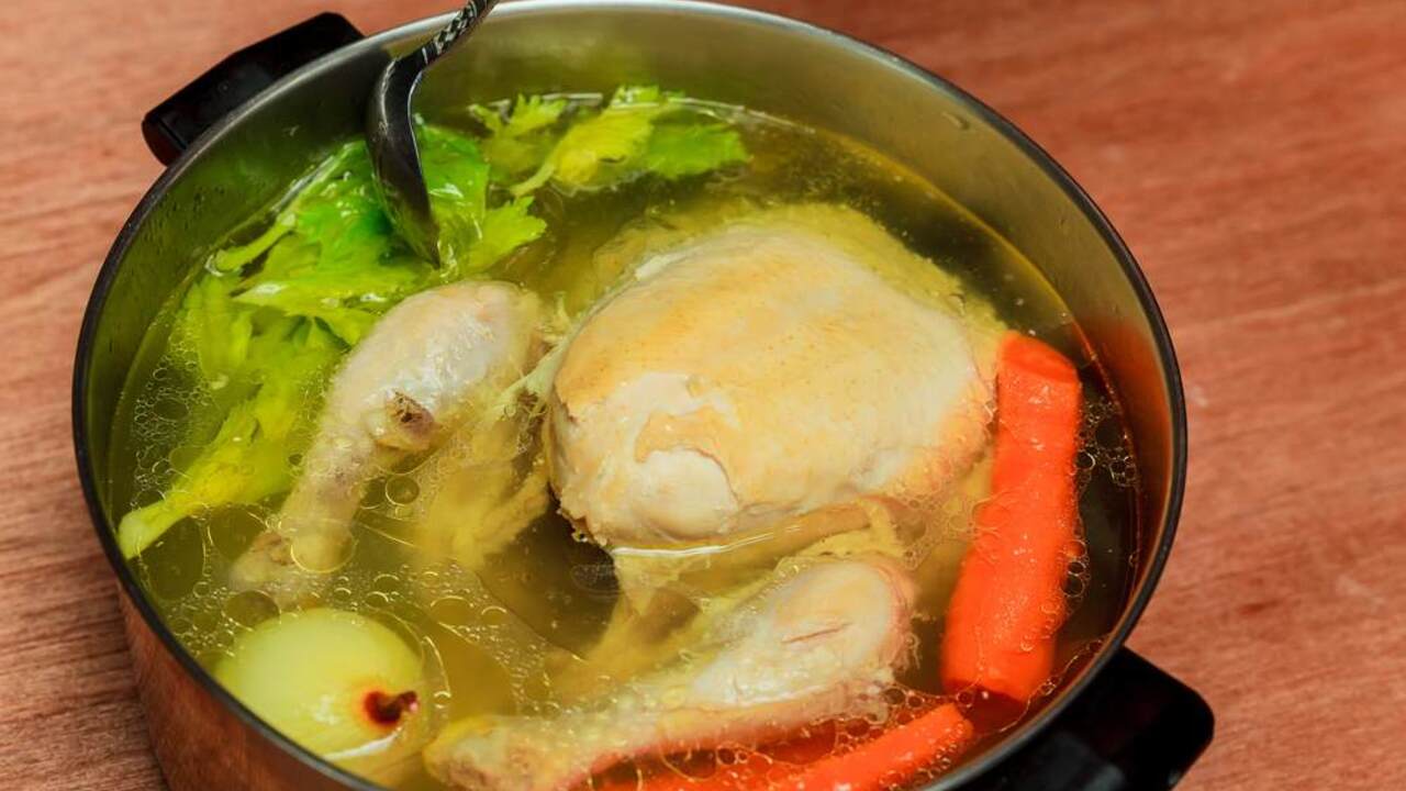 Domáca kuracia polievka s celým kusom kurčaťa, mrkvou, zelerom a cibuľou variaca sa v hrnci.