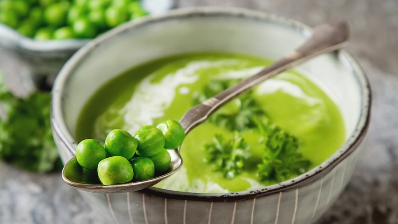 Krémová hrášková polievka v miske s lyžicou plnou zeleného hrášku.