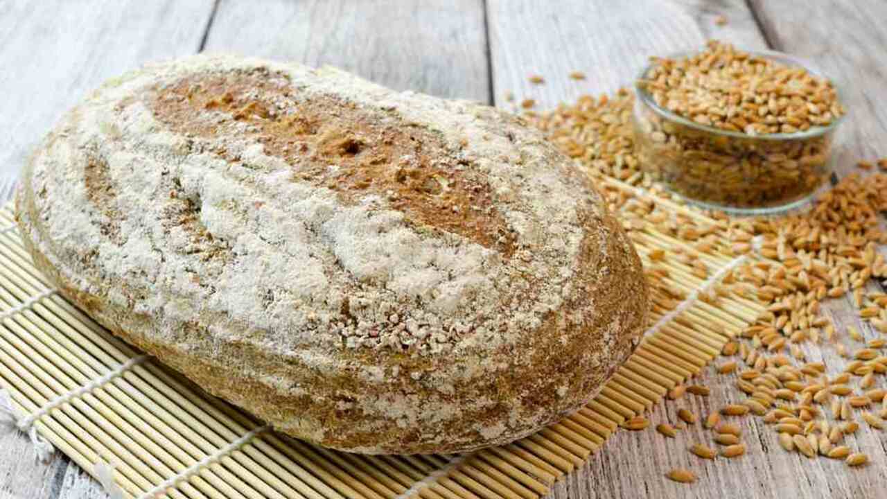 Domáci špaldový chlieb s chrumkavou kôrkou, položený na drevenom stole vedľa zŕn špaldy.