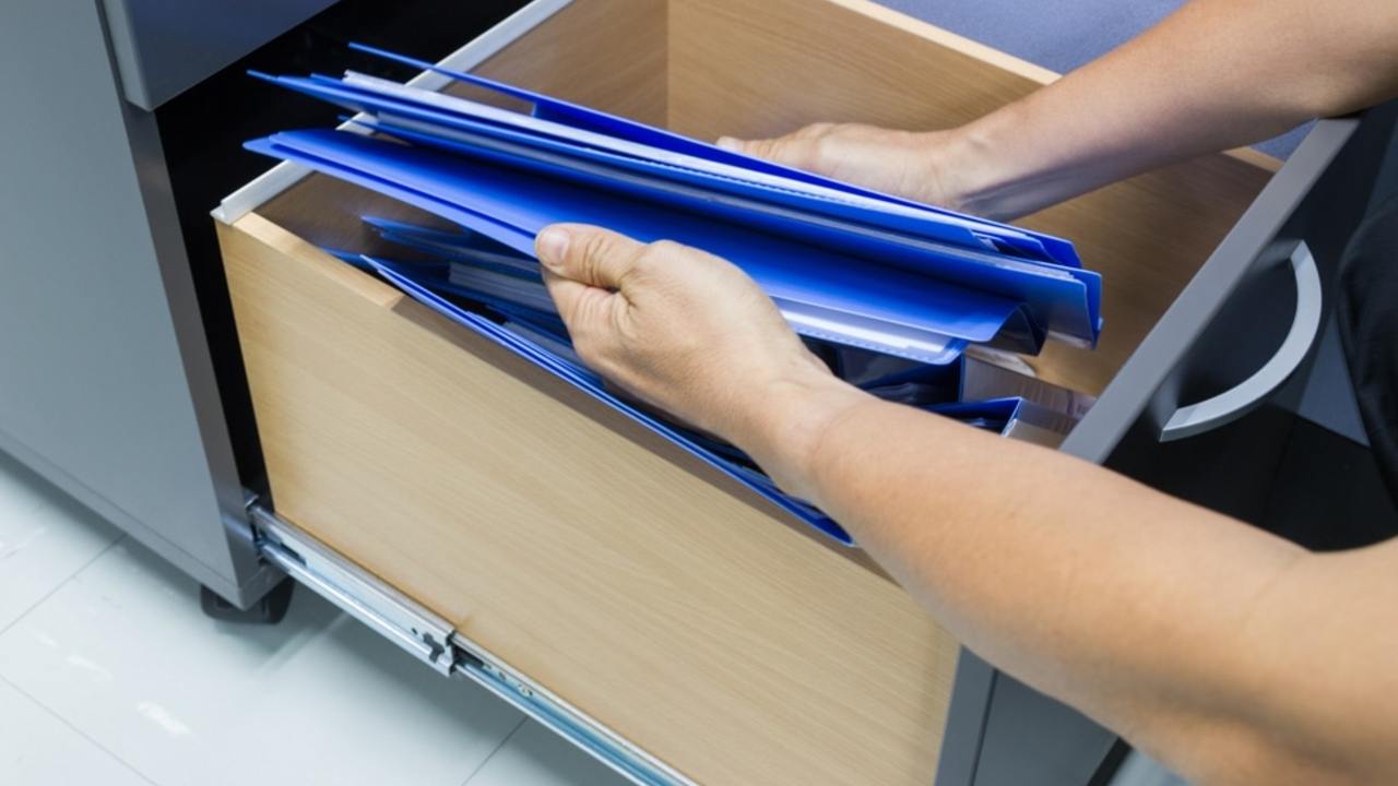 Ruky ukladajúce dokumenty a šanóny do zásuvky s dôležitými papiermi v domácnosti.