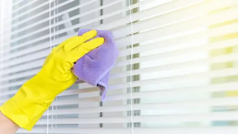 Žena čistí žalúzie mikrovláknovou handričkou zhora nadol.