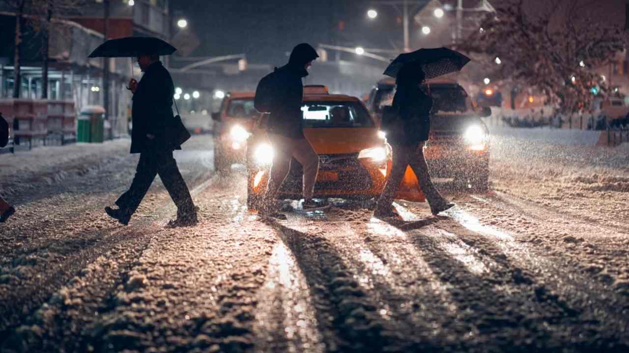 Chodci prechádzajú cez zasnežený priechod pre chodcov v rušnom meste v noci