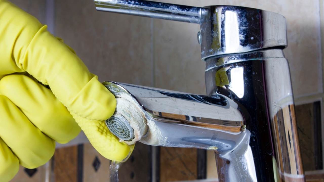 Čistenie zaneseného perlátora prekrytého vodným kameňom pomocou gumovej rukavice.