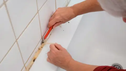 Zoškrabávanie zmäkčeného silikónu z okraja vane po použití domácej zmesi.