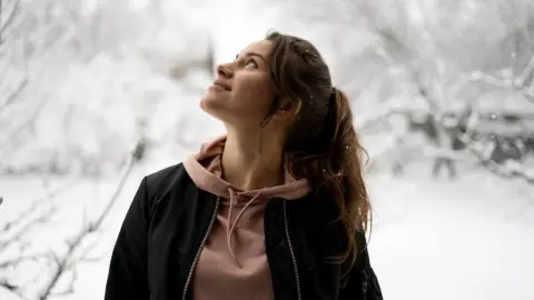 Žena stojaca v zasneženej prírode pozerá smerom hore, symbol mentálnej rovnováhy a vnútorného pokoja