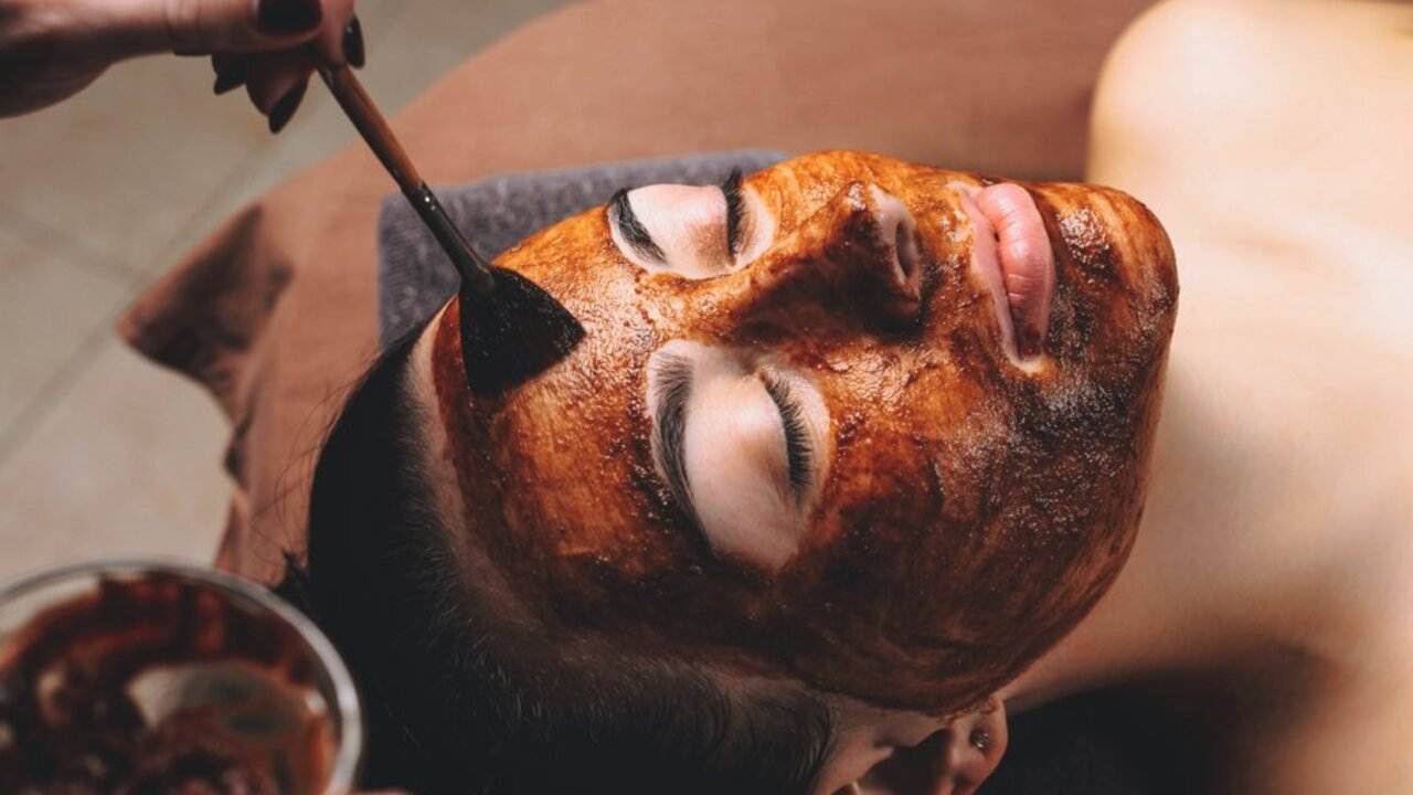 Žena počas relaxačného spa rituálu s kakaovou pleťovou maskou nanášanou štetcom.