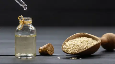 Sezamový olej v sklenenej fľaštičke so sezamovými semienkami ako prírodný elixír pre pokožku
