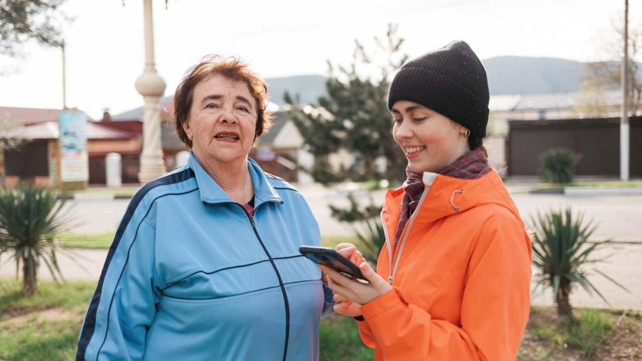 Mladá žena sa rozpráva so staršou pani na ulici a drží v ruke mobil počas krátkeho rozhovoru