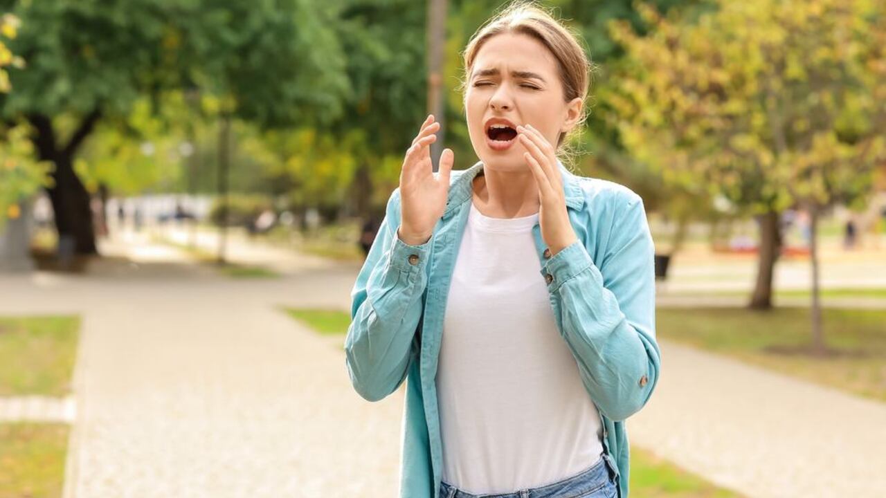 Žena na prechádzke v parku potláča kýchanie a zakrýva si ústa