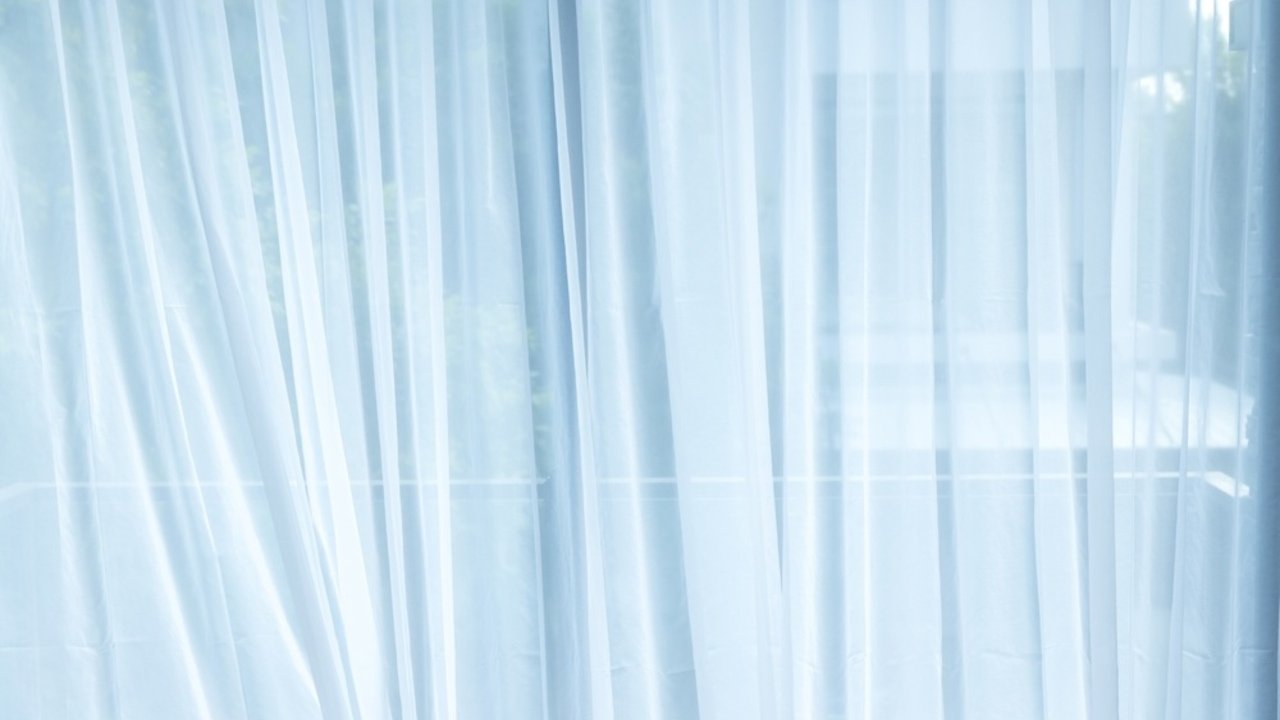 Svetlé biele záclony na okne, jemne presvetlené denným svetlom.