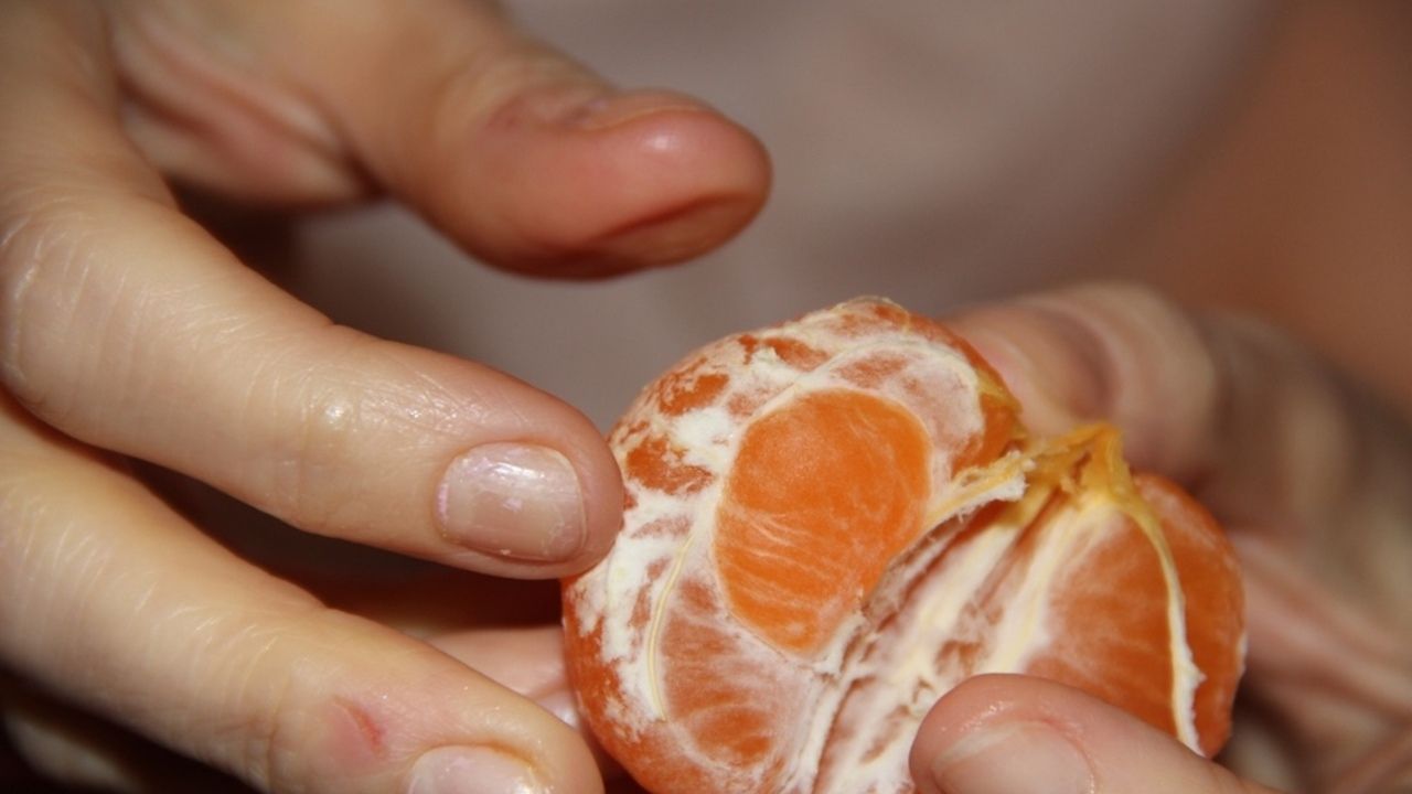 Ruka držiaca ošúpanú mandarínku s viditeľnými bielymi vláknami albeda.
