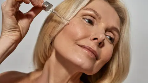 Žena po štyridsiatke nanáša skvalán na pleť pipetou počas zimnej starostlivosti