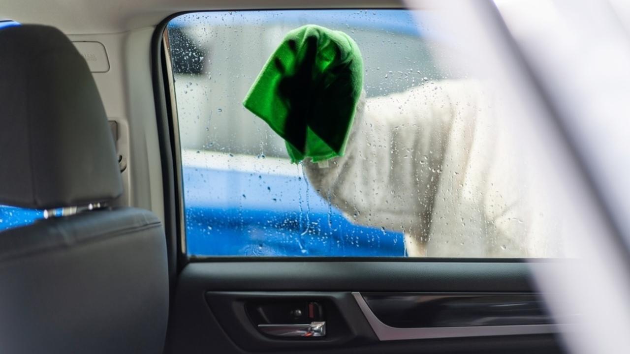 Čistenie zahmleného okna auta zvnútra pomocou handričky počas daždivého dňa.