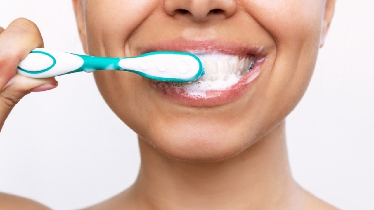 Žena si čistí zuby pred zrkadlom počas rannej hygieny.