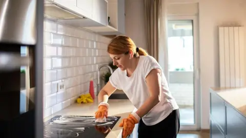 Žena upratuje kuchyňu a čistí varnú dosku v modernom interiéri