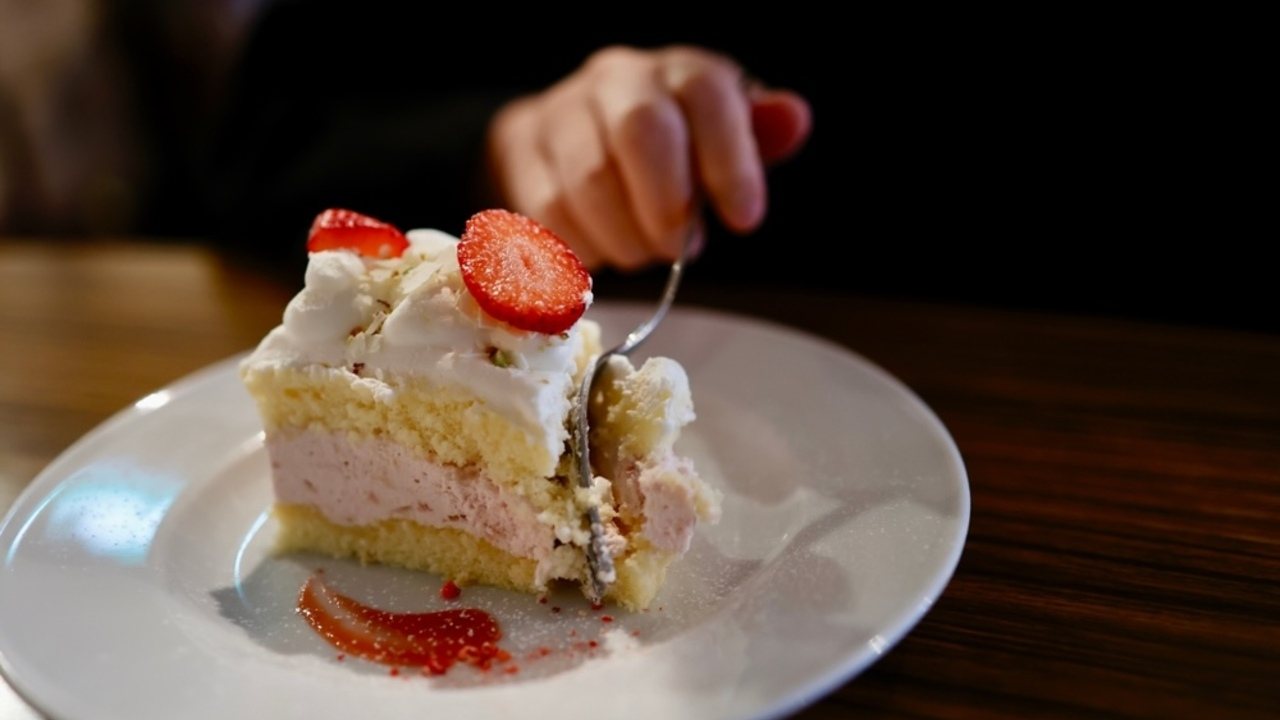 Kúsok jahodového koláča na tanieri, ktorý si človek naberá lyžičkou – detail sladkého dezertu.