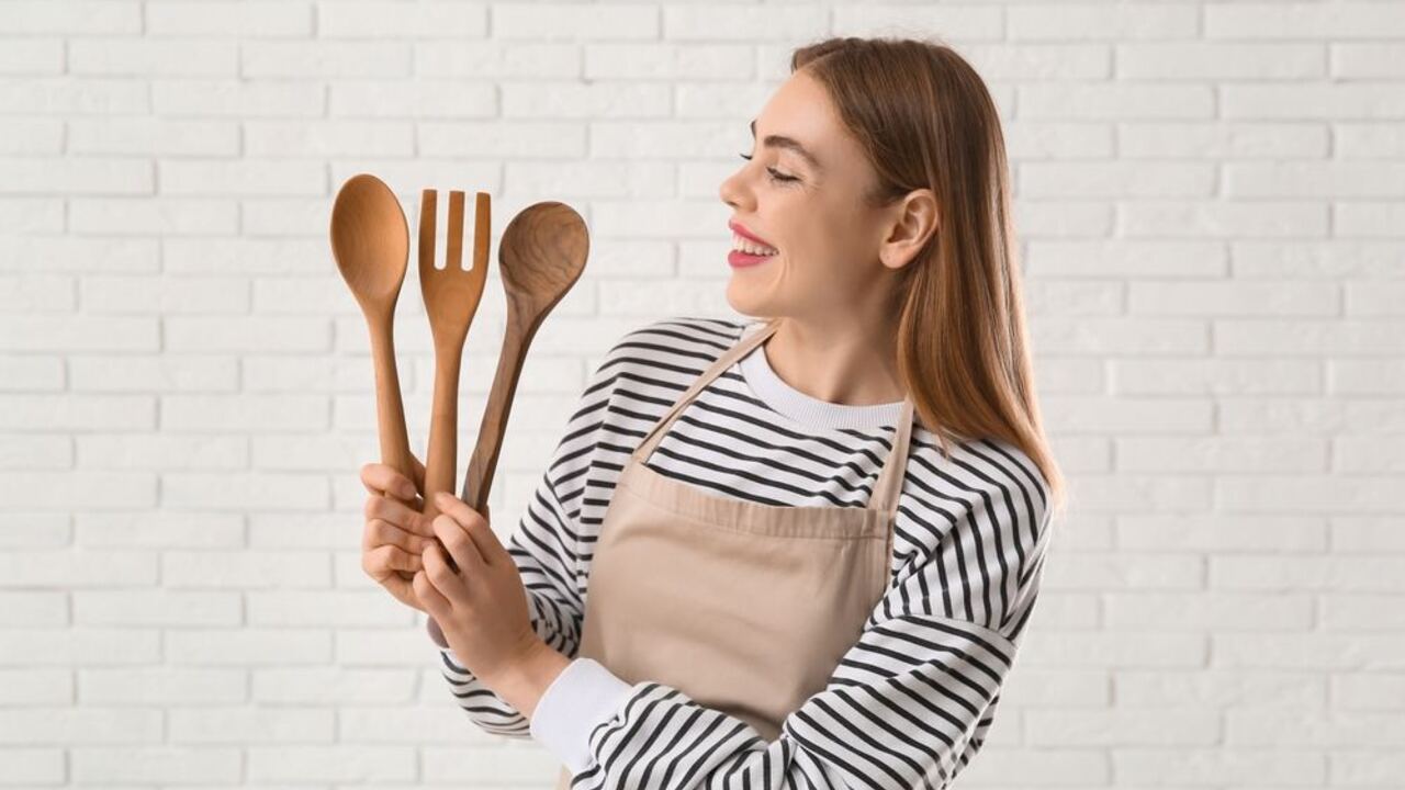 Žena v kuchynskej zástere drží v rukách drevené varechy a usmieva sa