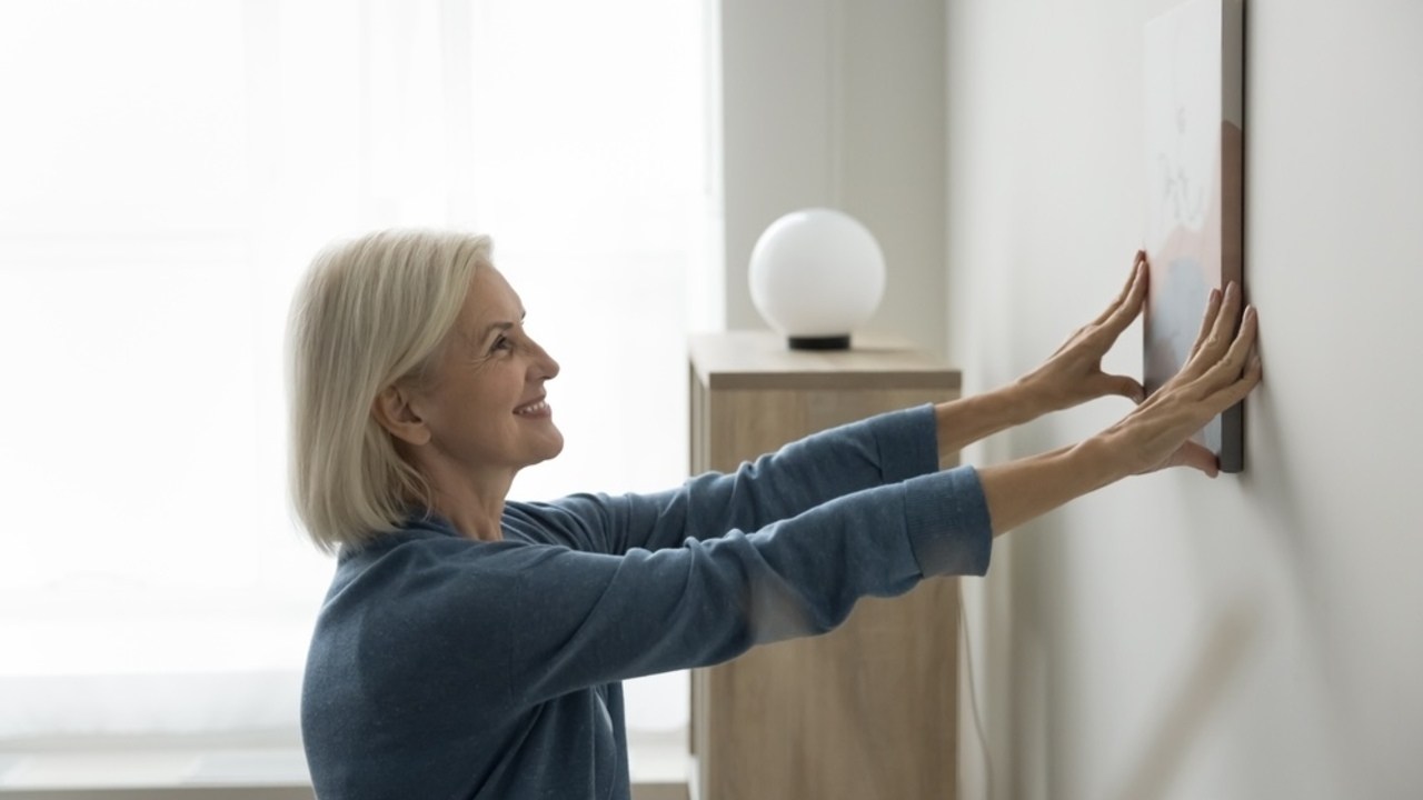 Žena upravuje rámiky na stene vo svojom byte