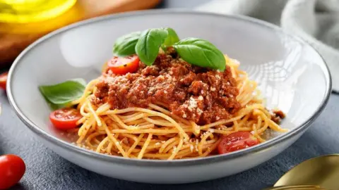 Špagety s boloňskou omáčkou podávané s parmezánom, cherry paradajkami a čerstvou bazalkou.