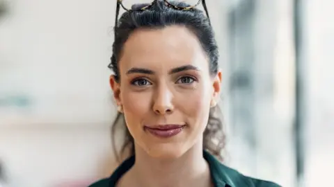 Sebavedomá mladá žena s okuliarmi na hlave, ktorá pôsobí premýšľavo a inteligentne.